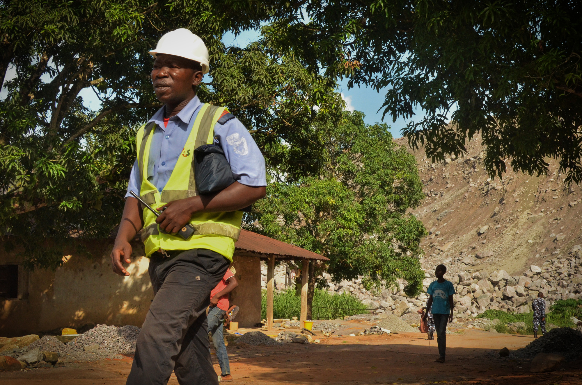 Koidu residents living within the mine's 500-meter safety zone are escorted by police and private security officers to safety checkpoints, where they wait for the mine's bi-weekly blasting to pass. 