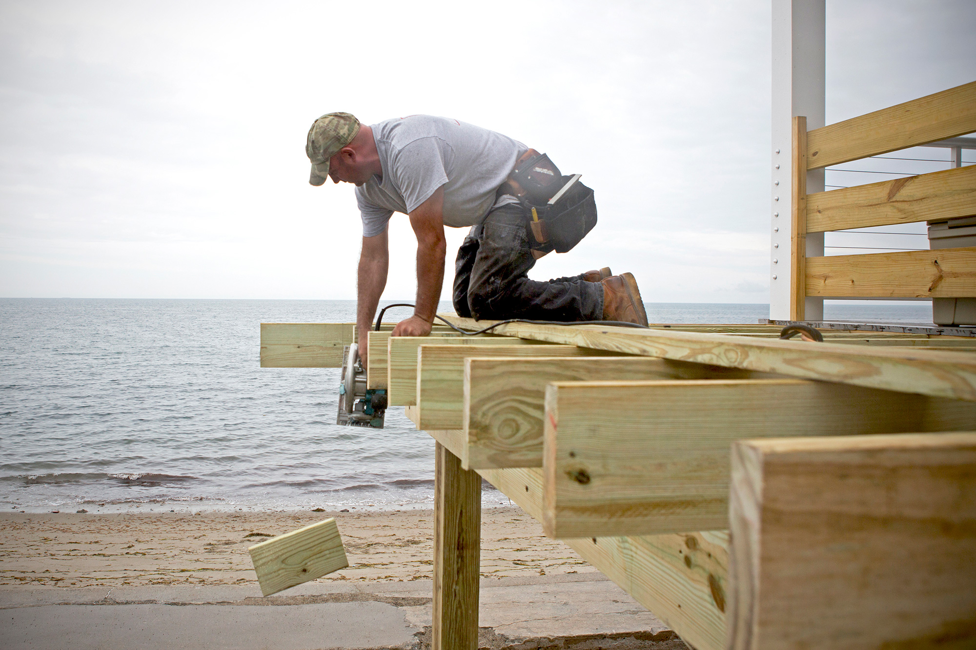 Fourth generation construction worker, Chris Pratt, of Pratt Custom Building, works on the deck of a raised home in Scituate. Business booms for Pratt during the summer months, when homeowners rebuild their houses after storms and prepare for future severe weather. (Photo by Lauren Owens Lambert/GroundTruth)