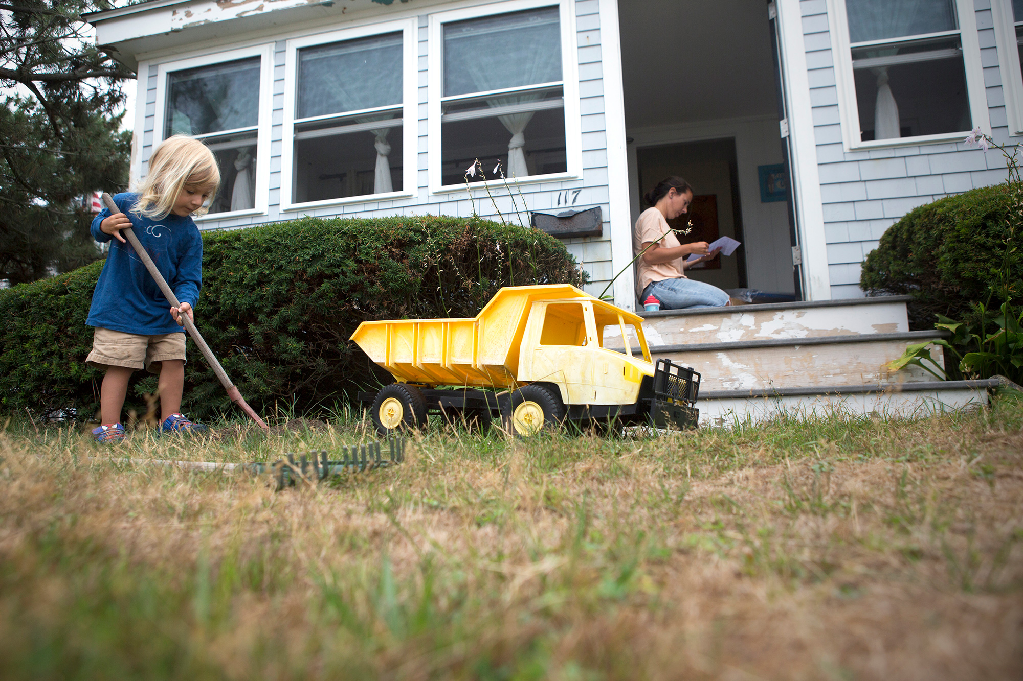 Scituate resident Devon Barrie and her son, Kailub Sullivan, live along the beach in Scituate near the new town seawall under construction. Sullivan likes to imitate the working crew with a toy dump truck, moving dirt from one side of the yard to the other. (Photo by Lauren Owens Lambert/GroundTruth) 