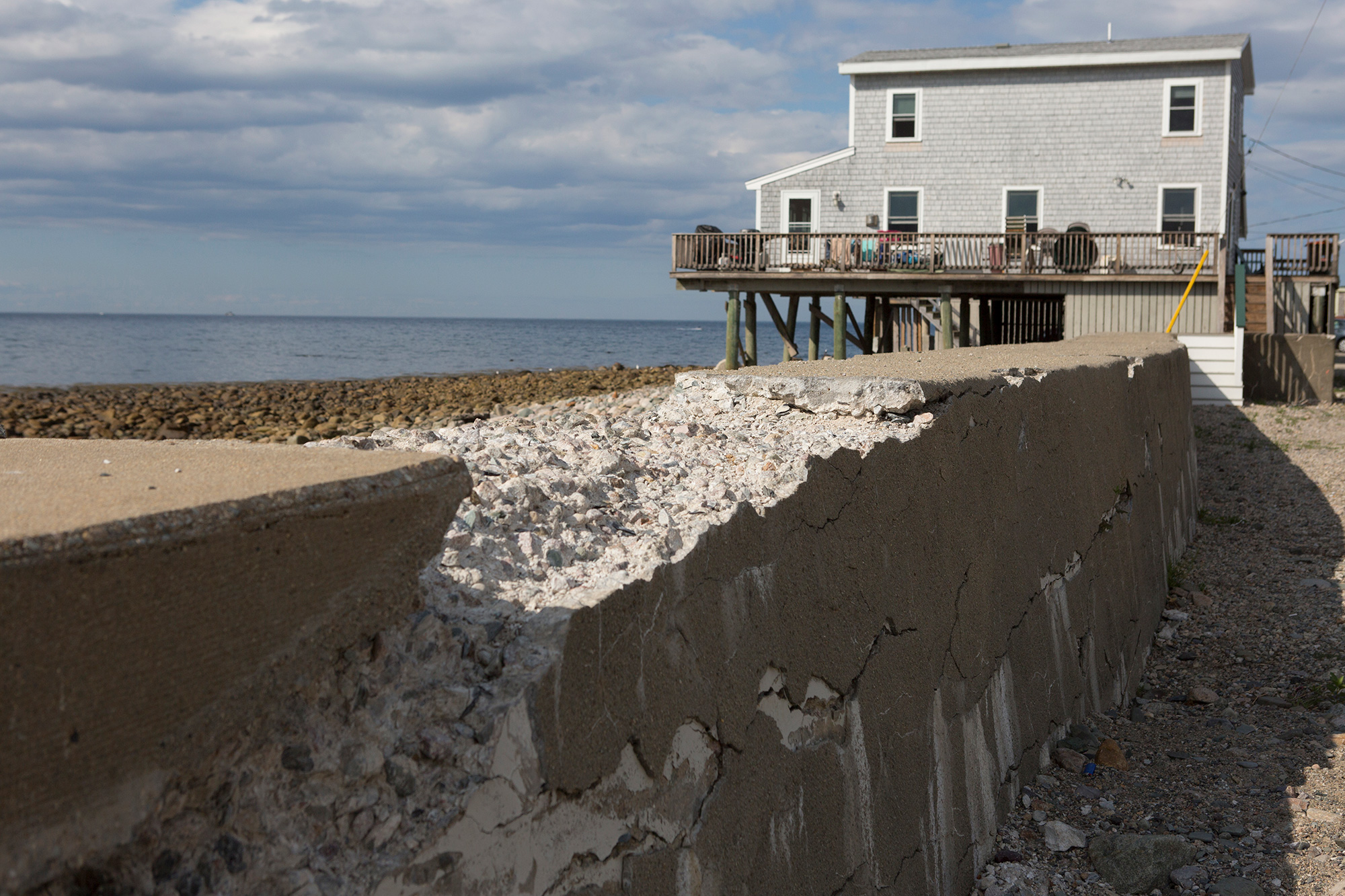 Next to a raised home in Scituate, a seawall crumbles—the result of years of ocean waves pummeling the shores. Most coastal towns along the Massachusetts South Shore have man-made sea walls in place to help protect the ocean front from storm surges. But recent storms have breached the seawalls and weakened them for future storms. (Photo by Lauren Owens Lambert/GroundTruth)