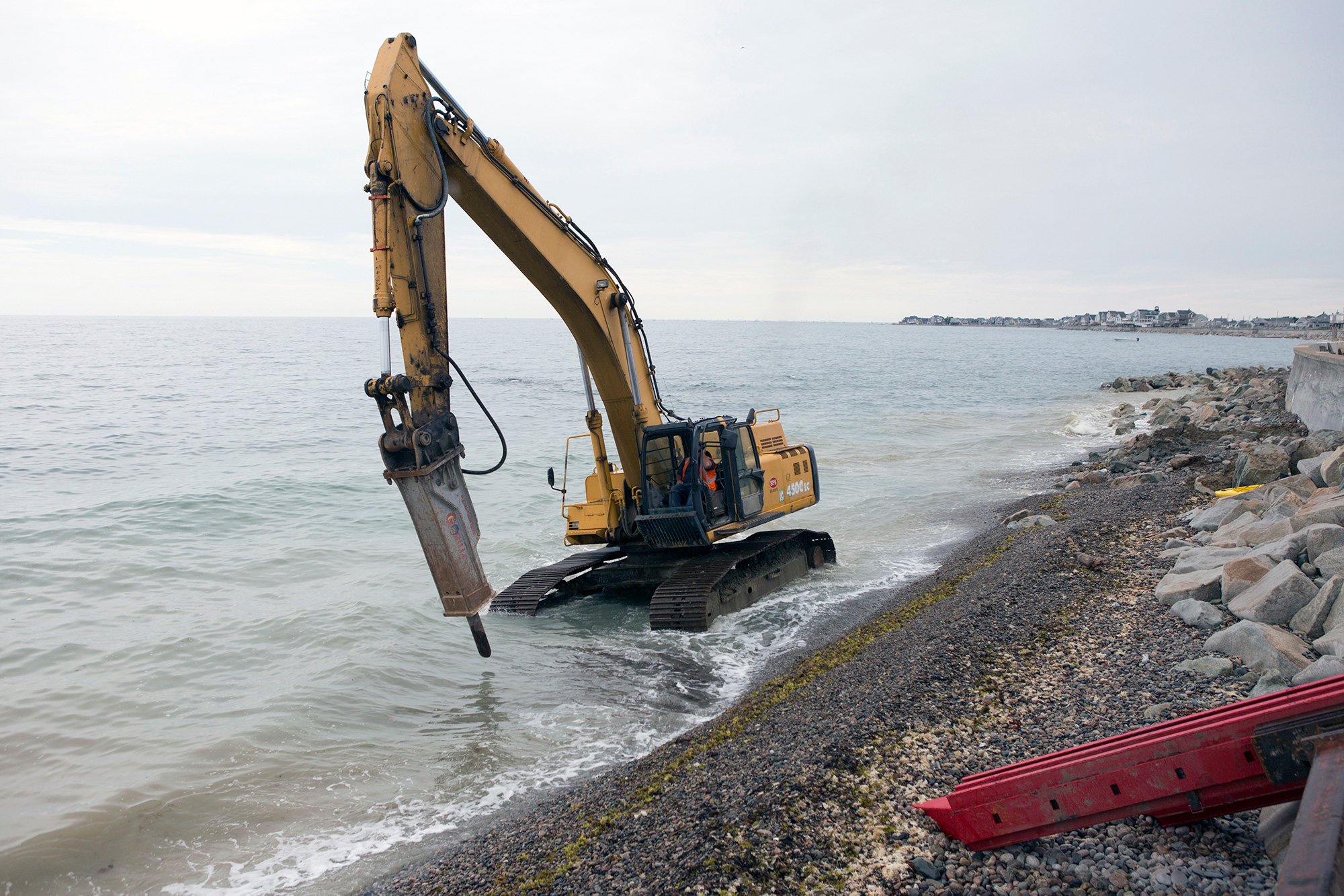 A wheel excavator travels up the rocky shore south of Egypt Beach in Scituate as construction workers rebuild a damaged seawall, originally built in the 1930s. The crew is increasing its height and strength with additional steel support and rocks. (Photo by Lauren Owens Lambert/GroundTruth)