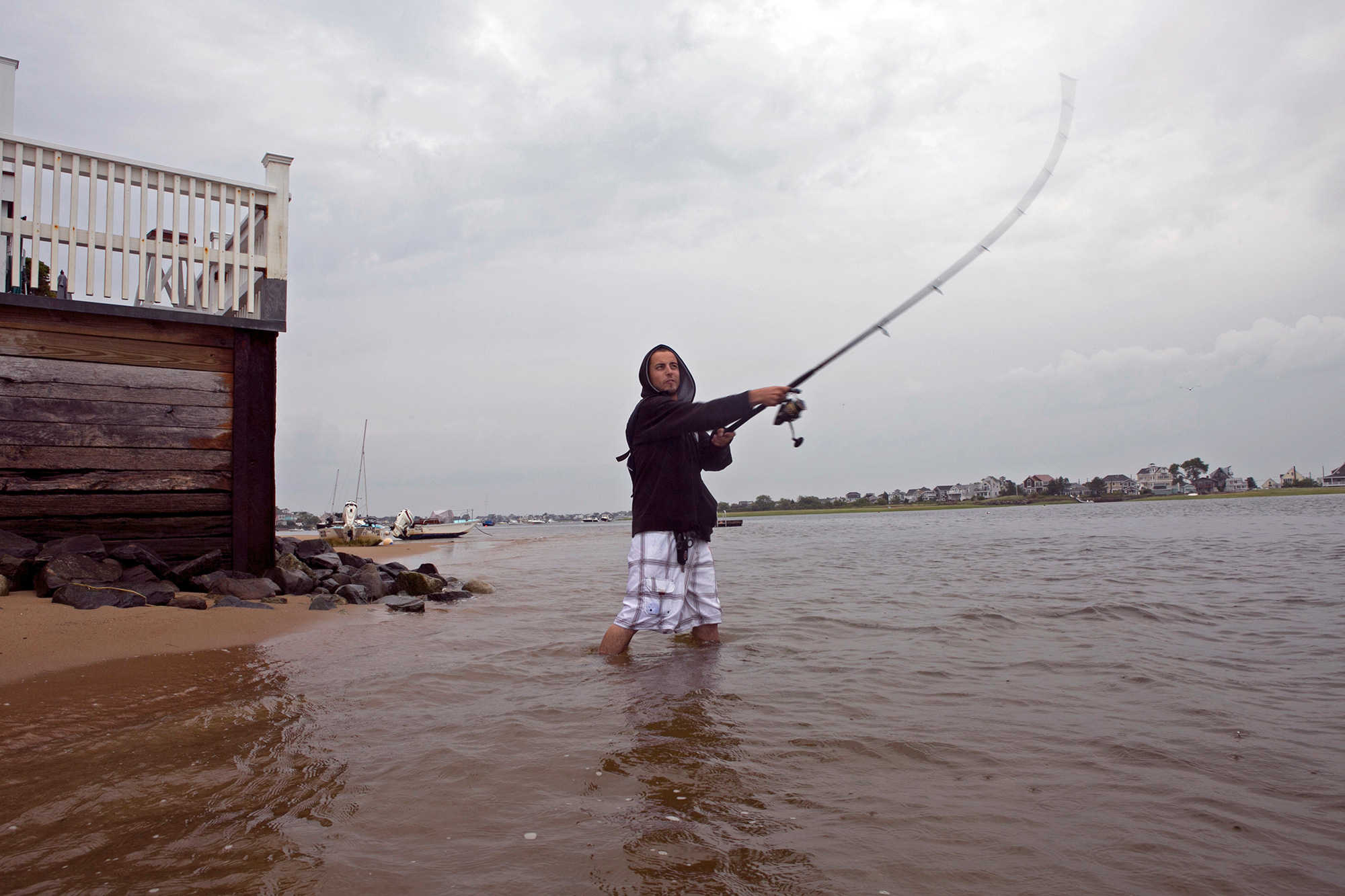 Marcos Rego fishes for striped bass on Plum Island early in the morning. During high tide, the water slaps against the building behind him. (Photo by Lauren Owens Lambert/GroundTruth)