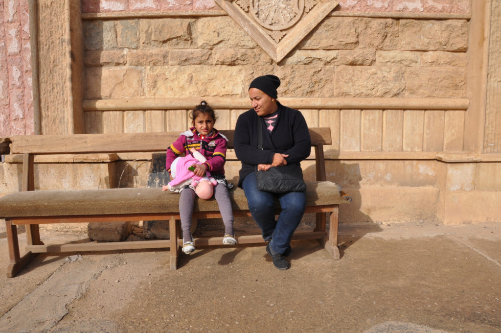 Saha and her daughter Mariam sit outside of their old church, now destroyed. (Photo by Lauren Bohn/GroundTruth)