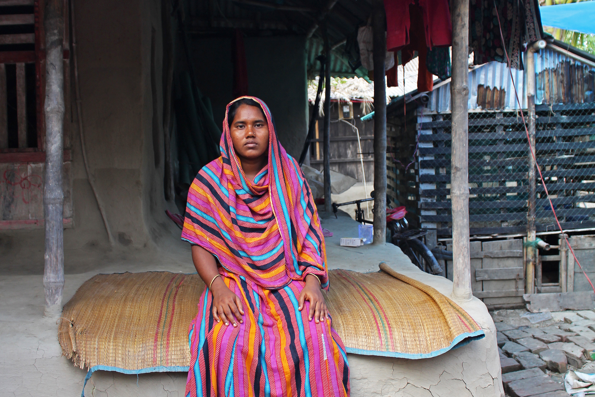 Romesa Khatun sits on her porch, an extension of the raised mud platform on which her house is built. Her home, like most others in the village, was completely destroyed during Aila, a devastating cyclone in 2009. (Photo by Neha Thirani Bagri/GroundTruth)