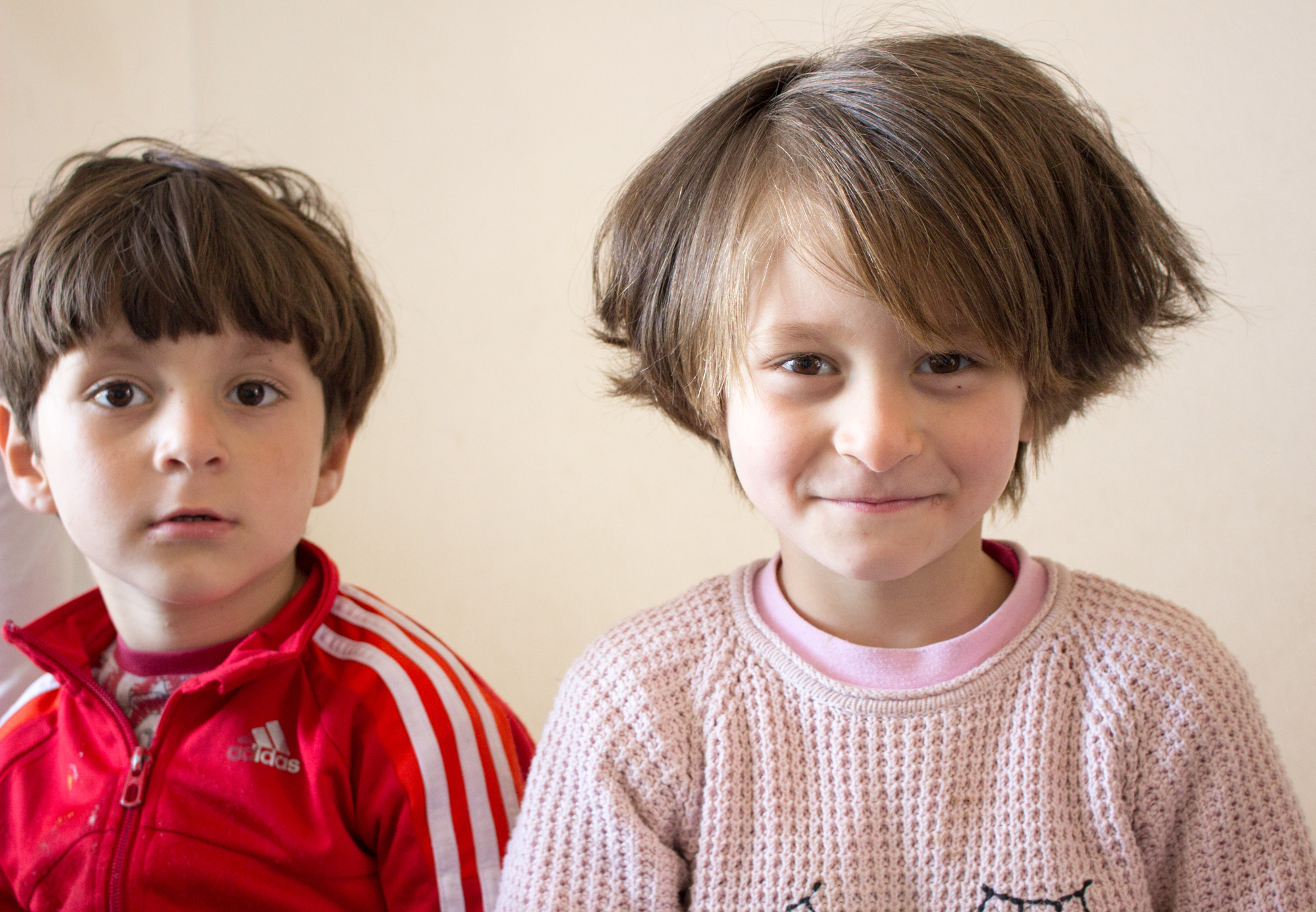 After running around outside, two of Alia Habesh’s children sit on a twin bed in their cramped, but tidy apartment in Sindos. They’re both recovering from tuberculosis, contracted while fleeing Aleppo, and enjoy playing with any visitors. (Photo by Catherine Clark/GroundTruth) 