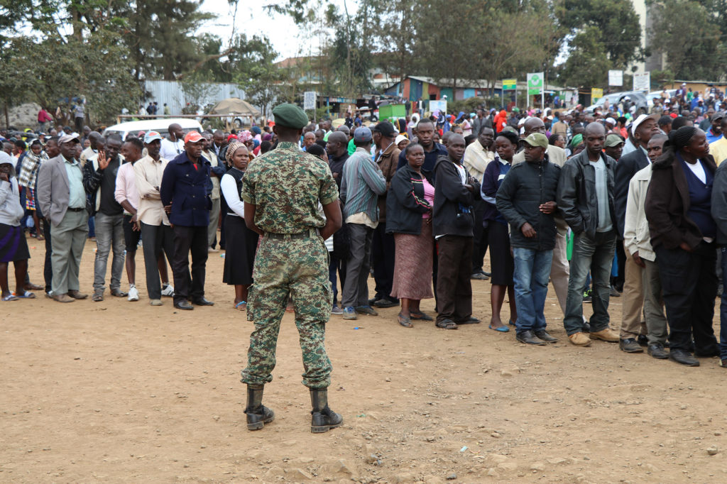 Over 180,000 police officers and security forces were deployed across Kenya to prevent violent riots. Here, a guard watches over long voting cues in Kibera slum, Nairobi. (Neha Wadekar/GroundTruth)