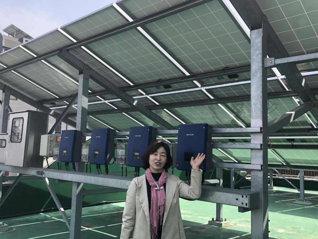 Eunsook Cho of Won Buddhist Eco Network stands in front of the solar panels on the roof of Song-cheon Won Buddhist temple in Seoul. (Sherry Simpson/GroundTruth)