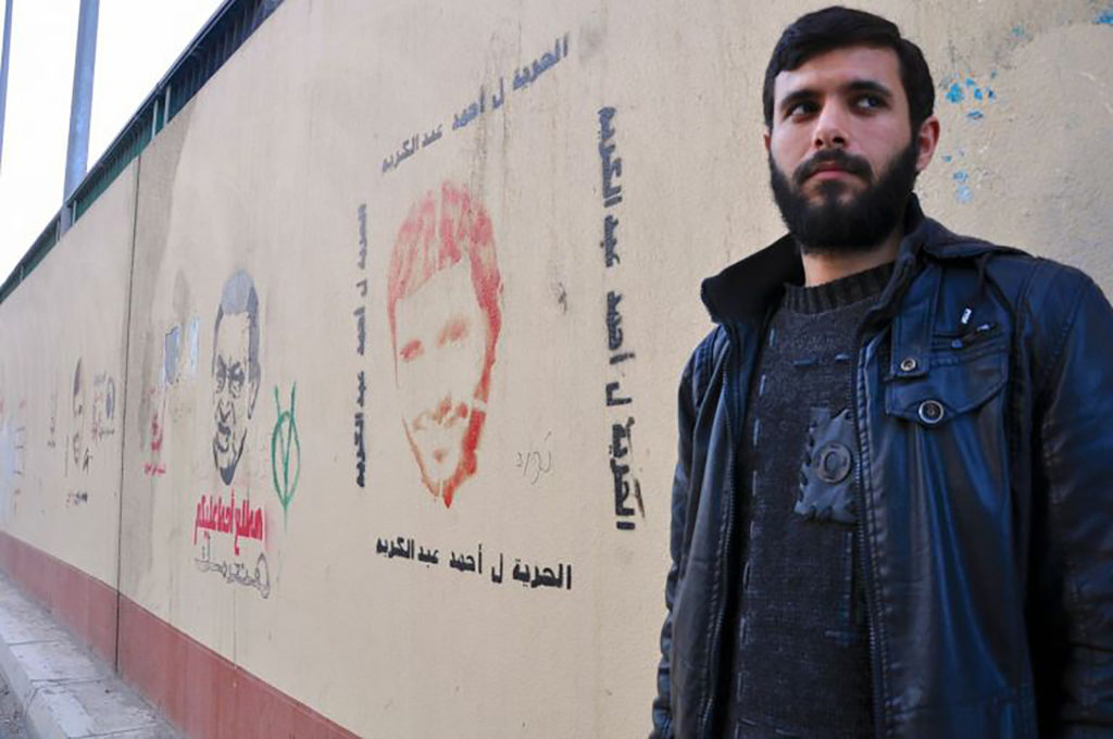 Ahmed in 2013, after he was released from prison for blogging anti-Mubarak critiques. He stands next to graffiti of his face, advocating for his freedom. (Lauren Bohn/GroundTruth)